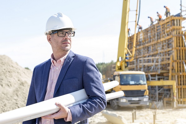 Confident architect holding rolled up blueprints at construction site